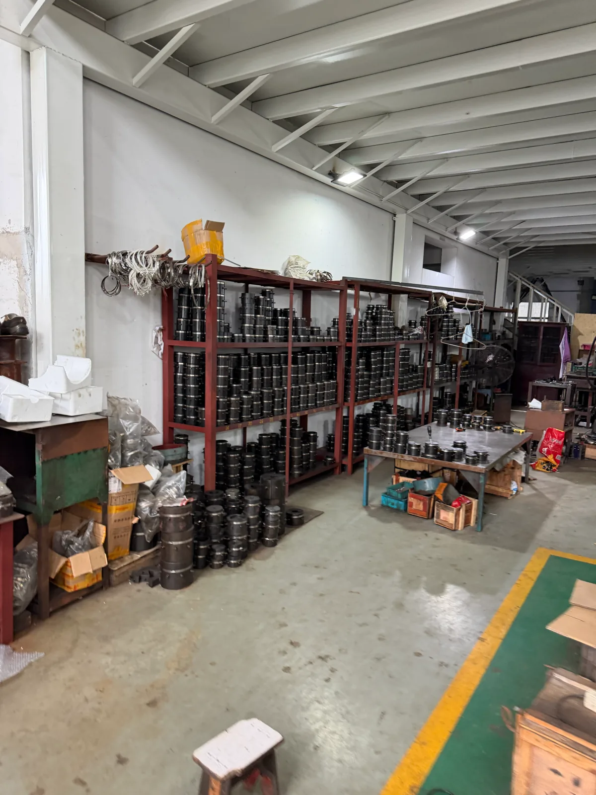 长货架和地面堆放大量黑色/金属圆柱件,车间通道完整